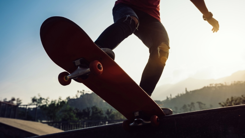 A skateboarder balances on a ledge at a skatepark during sunset